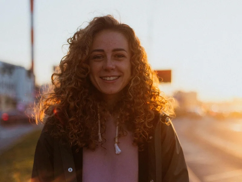Woman with curly hair smiling warmly in golden sunset light