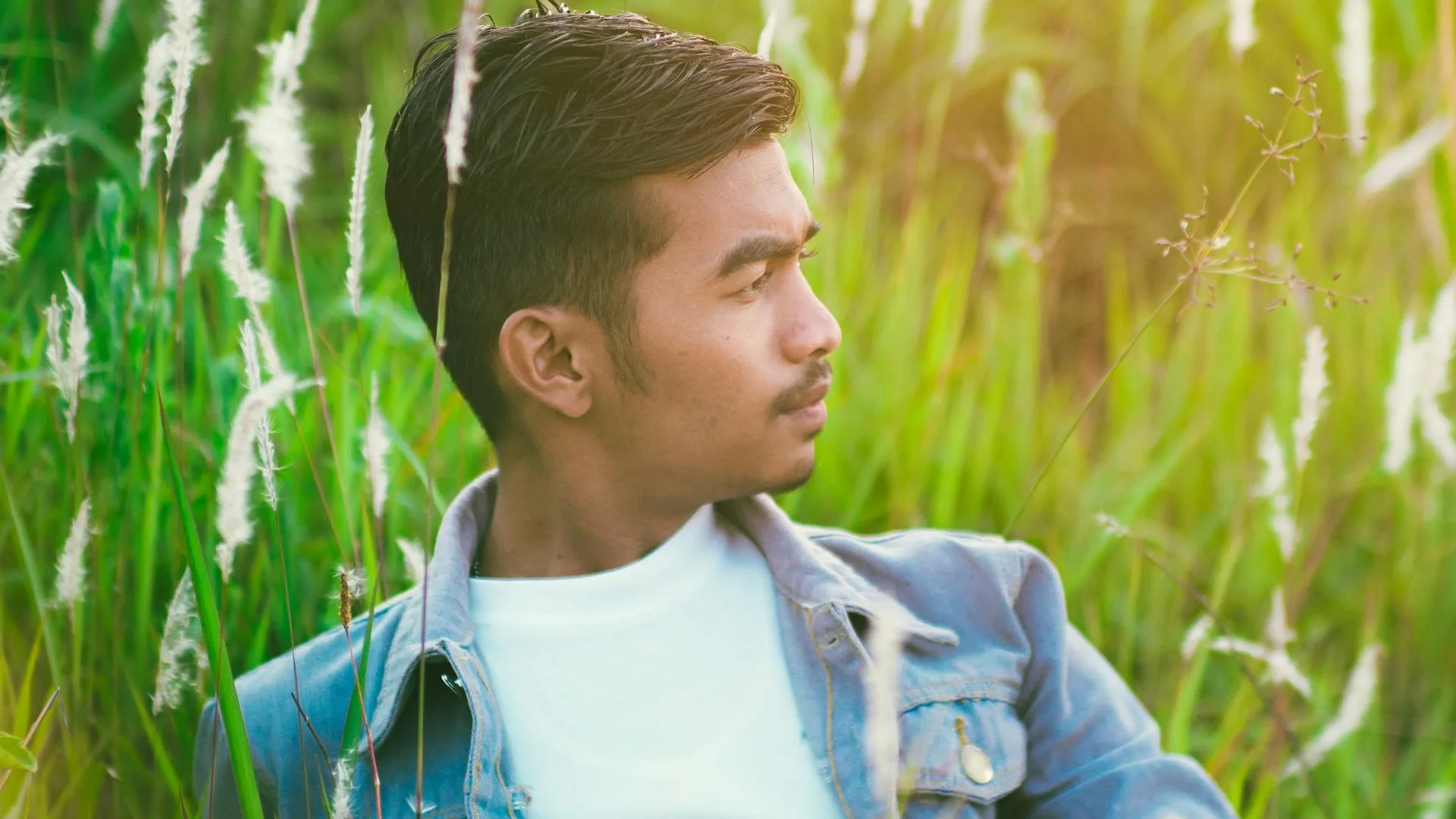 Young man in a denim jacket relaxing in a lush green meadow, enjoying nature's tranquility