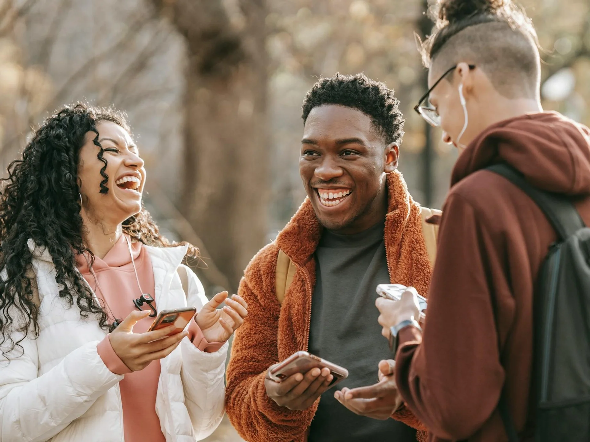 Cheerful multiracial friends laughing while browsing phones together