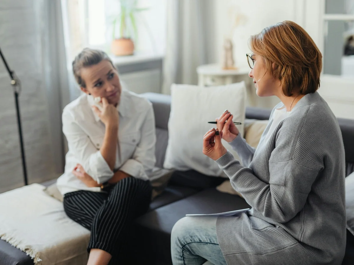 Two women in a thoughtful conversation on a couch in a cozy counseling setting