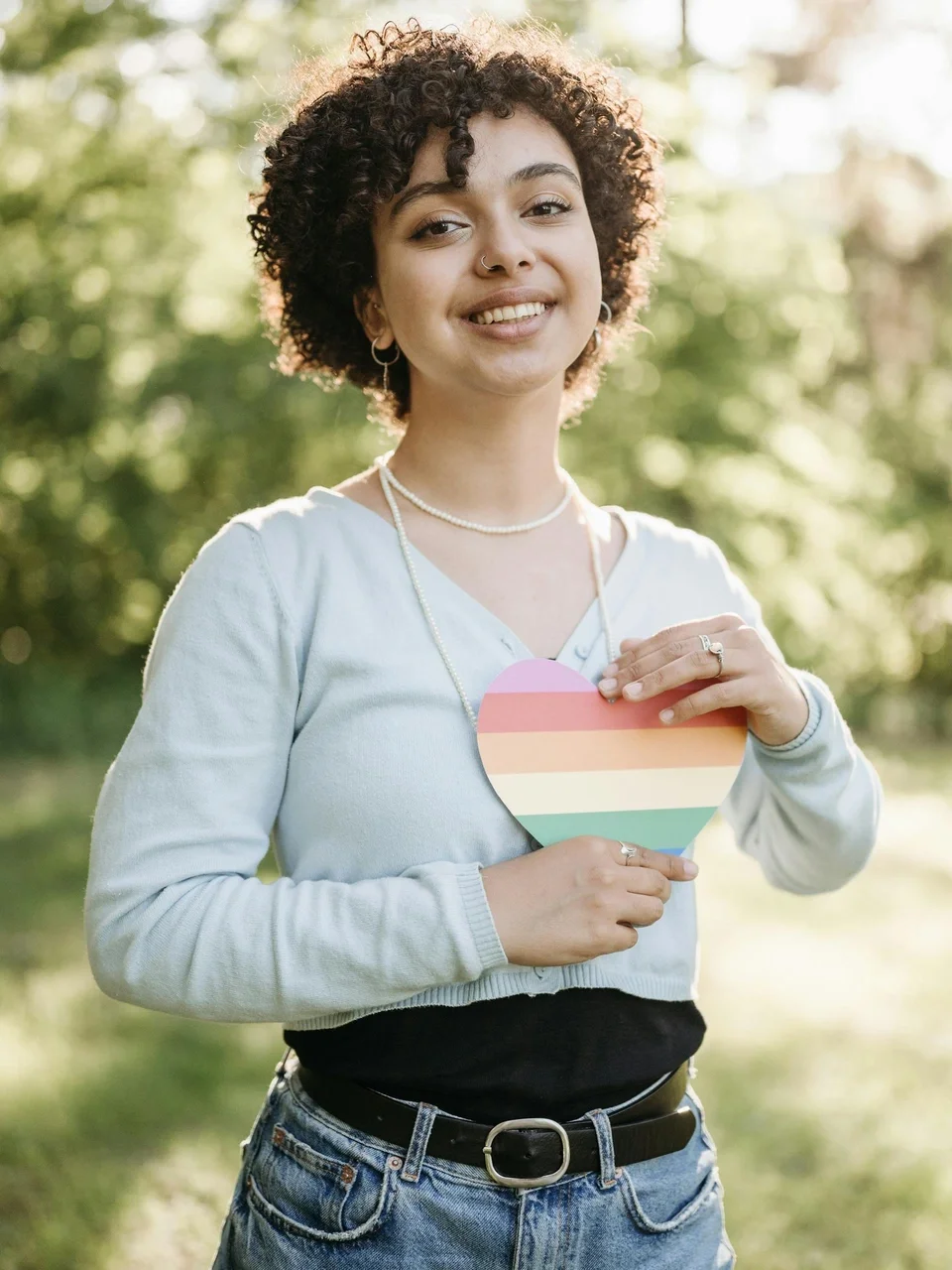 Cheerful woman holding a rainbow heart in a sunny park