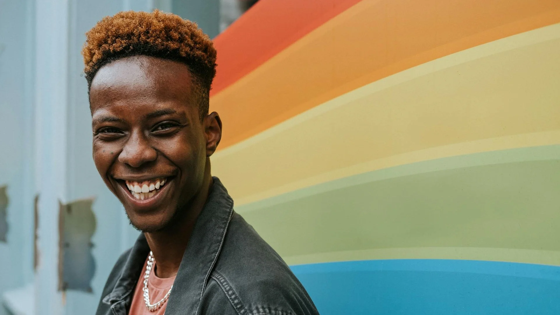 Cheerful young man smiling near a rainbow pride flag on the street
