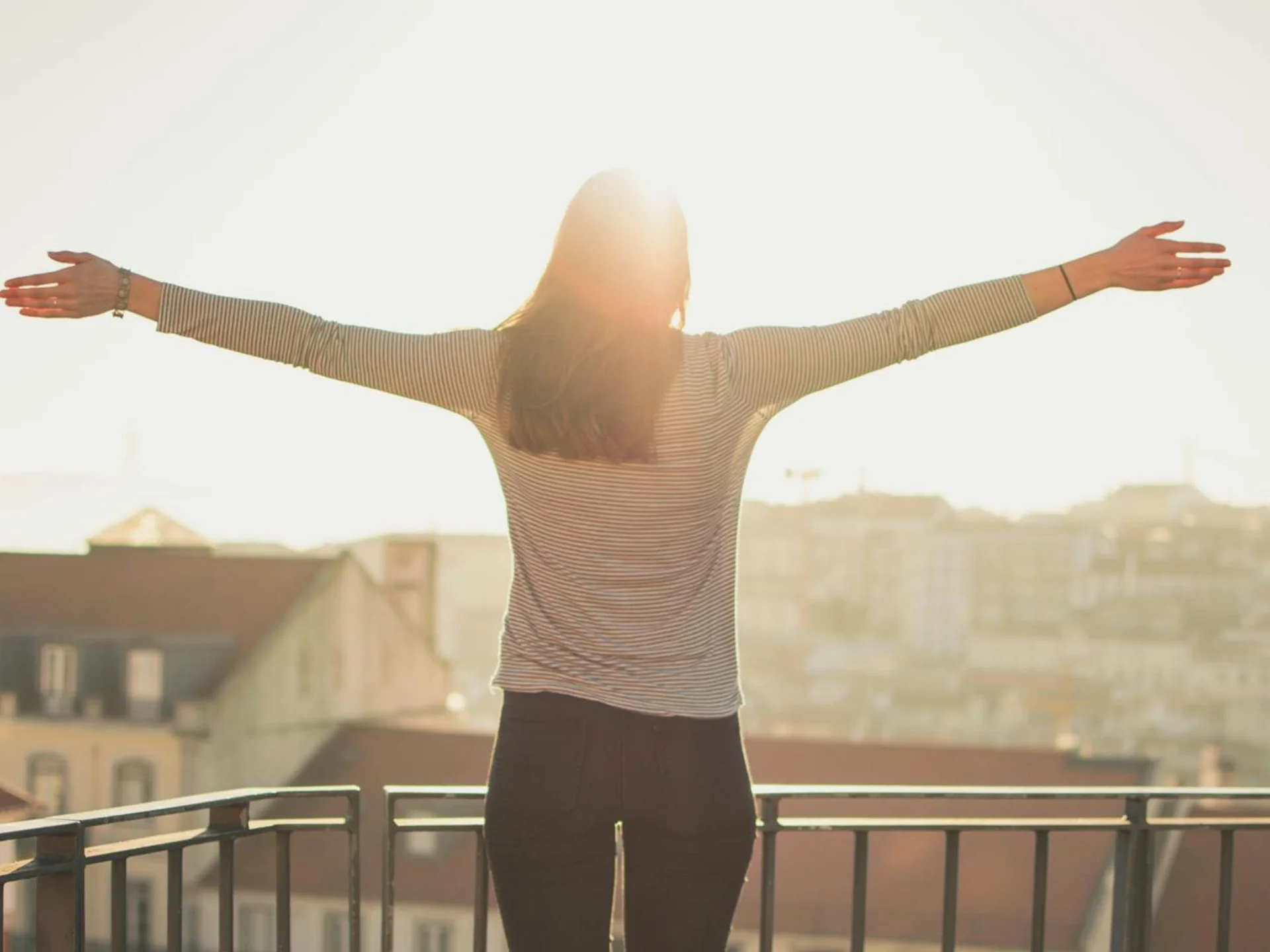 Woman standing with outstretched arms on a sunny balcony, embracing the morning light