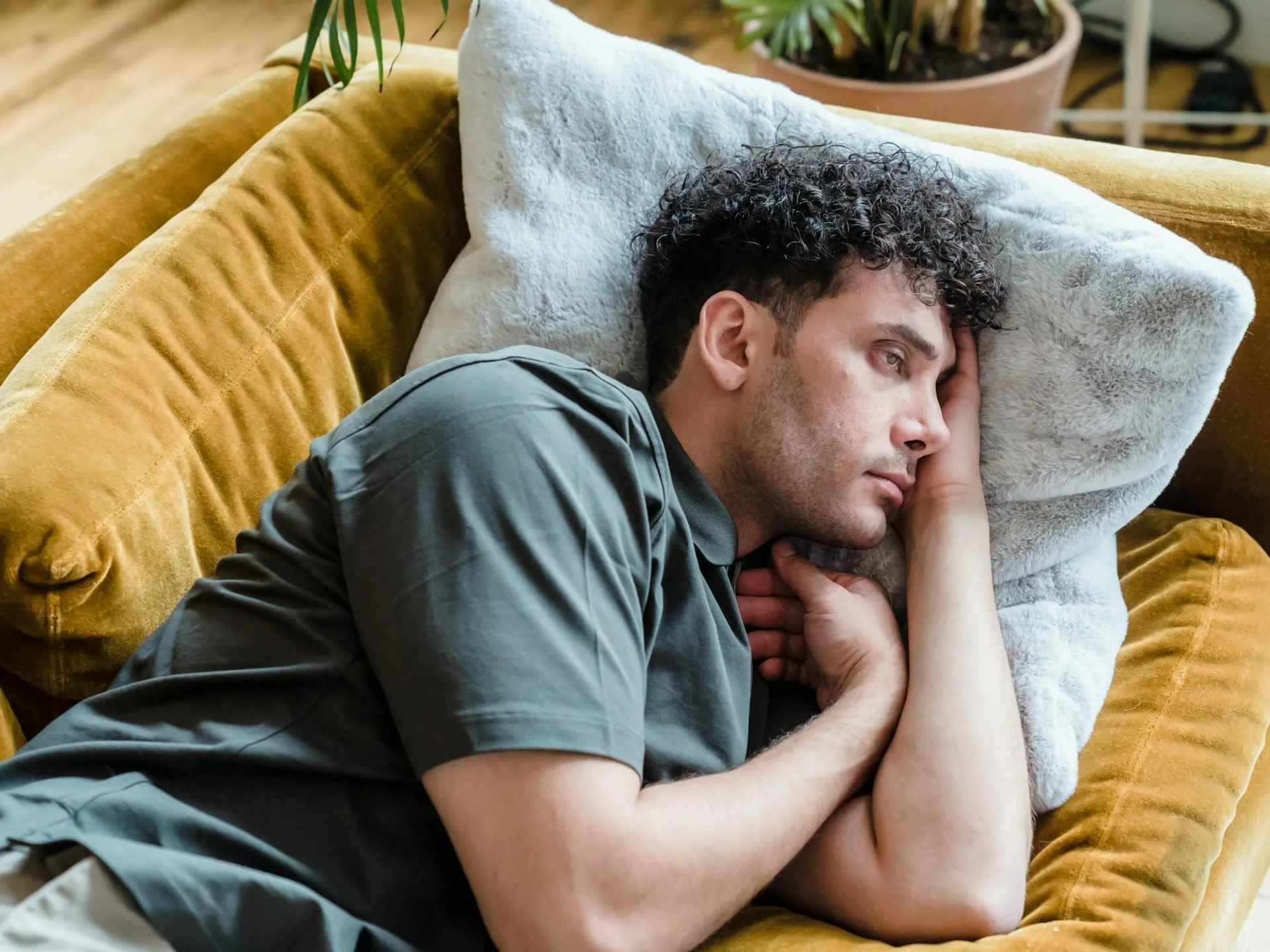 Thoughtful young man relaxing on a warm-toned couch with a soft pillow