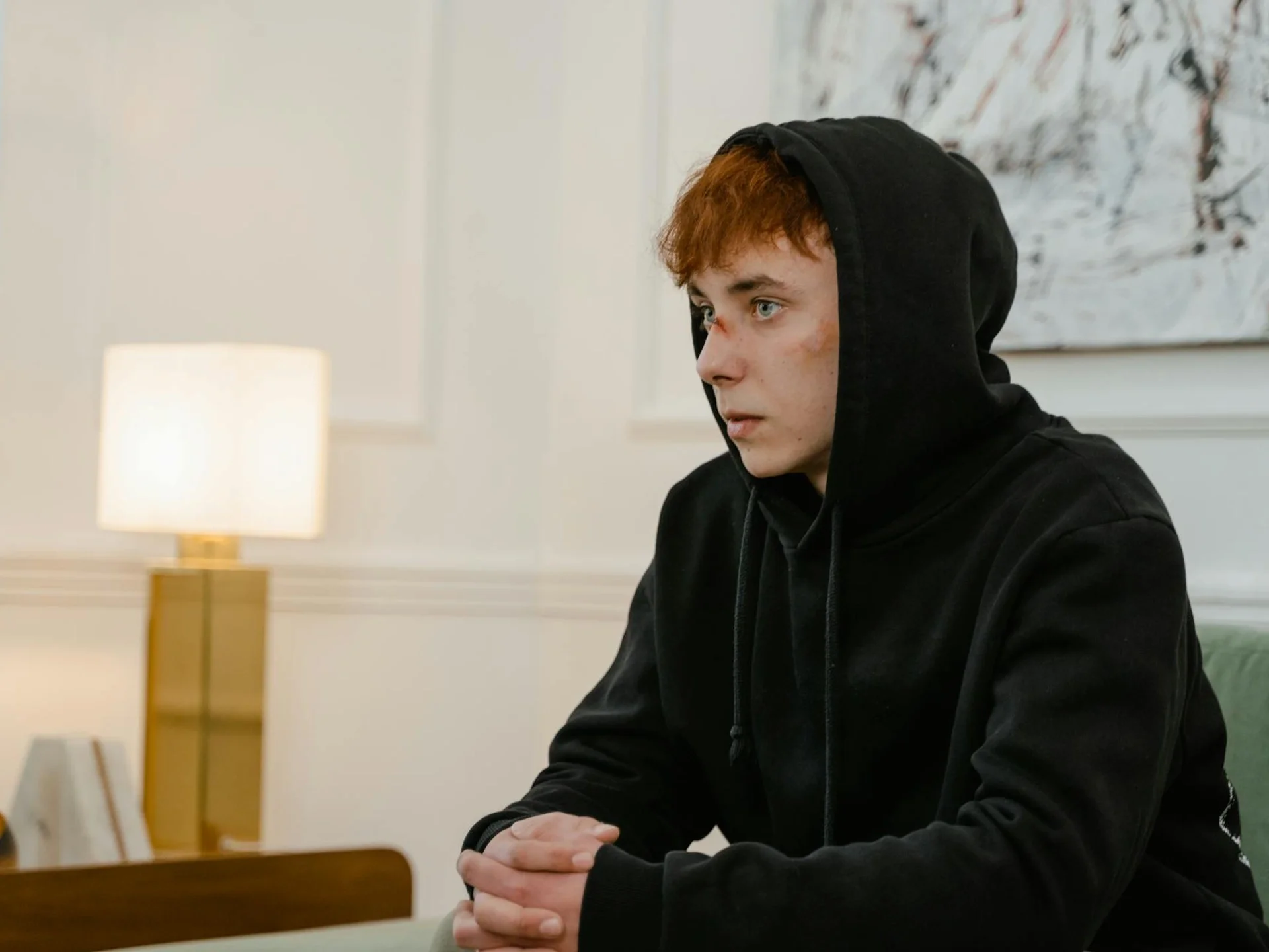 Teenager with bruises sitting indoors, deep in thought