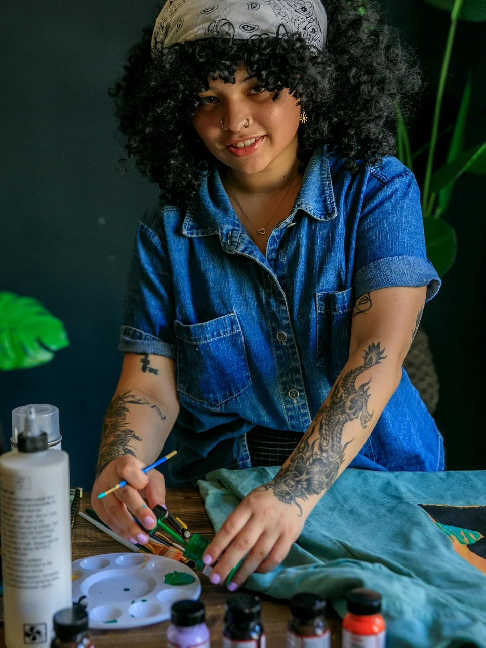 Young artist with tattoos painting at a table surrounded by plants