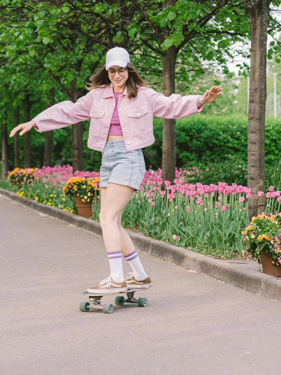 Young woman skateboarding along a vibrant park path lined with flowers