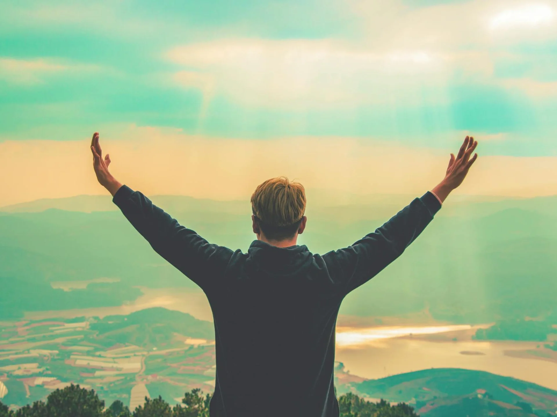 Person standing with arms raised, embracing the vast mountain landscape