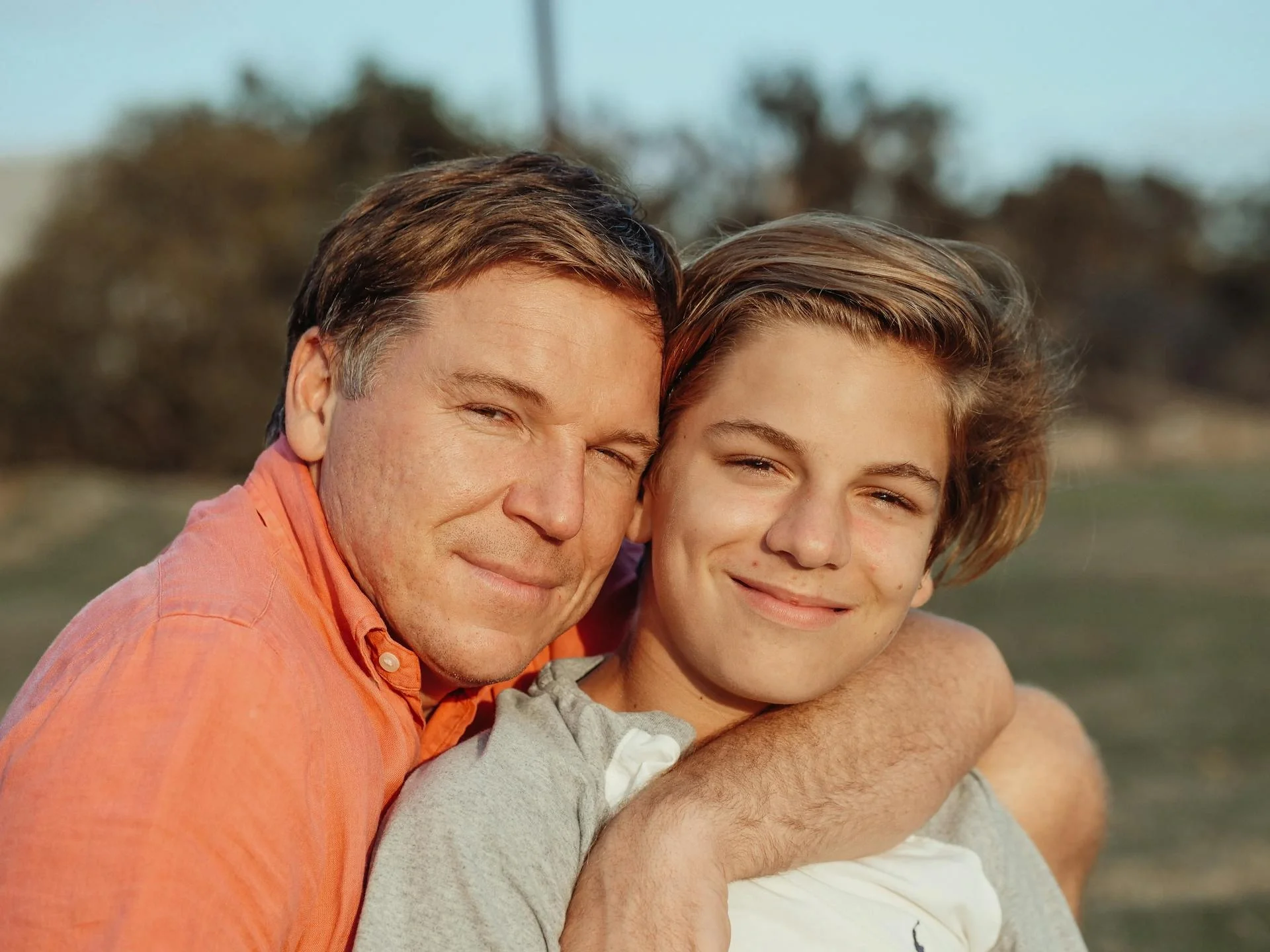 Father and teenage son sharing a joyful hug outdoors
